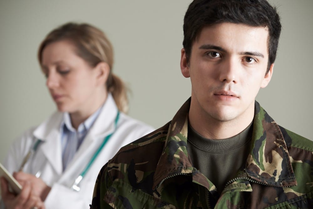 A man wearing camo with a doctor behind him taking notes