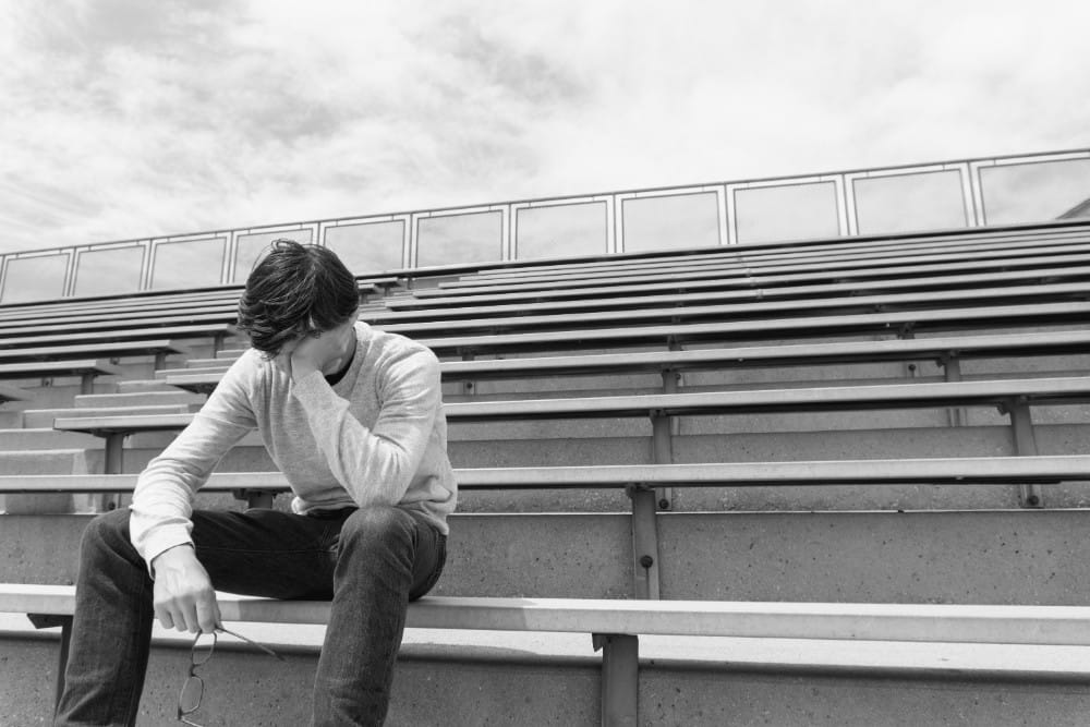 A boy sitting on bleachers with his hand on his head