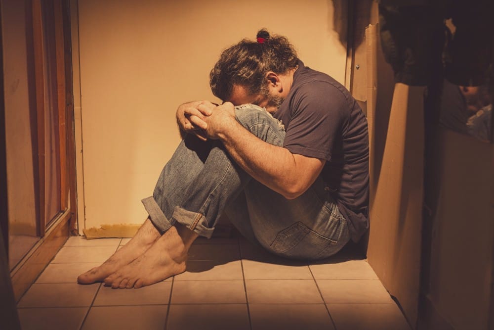 A man sitting in the corner with his head between his knees