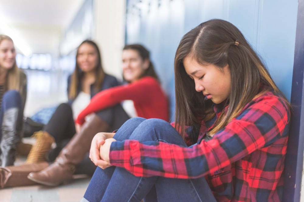 A girl sitting against a wall and girls behind her laughing